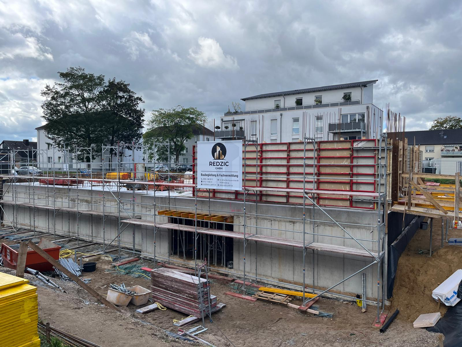 Rohbau eines Mehrfamilienhauses mit Stahlbetonwänden, Gerüst, roter Wandschalung und REDZIC-Bauschild