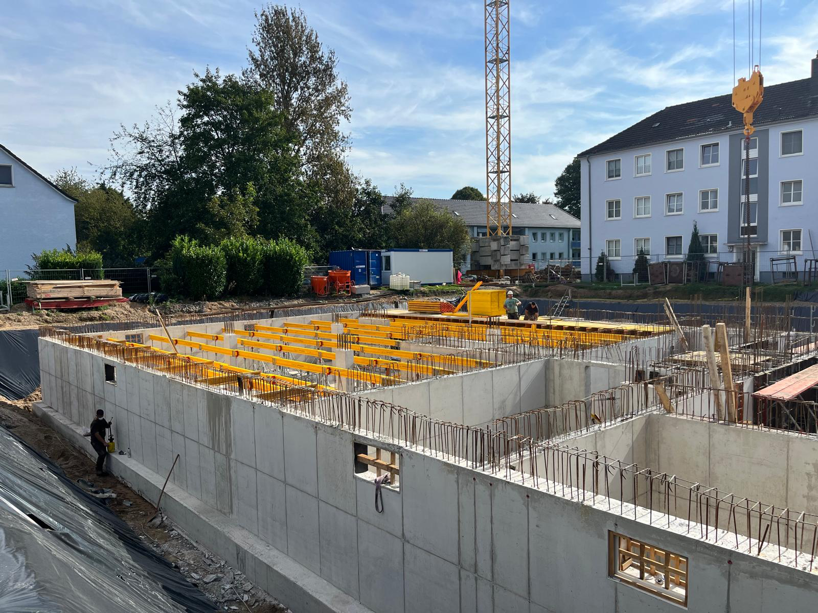 Kellergeschoss des Mehrfamilienhauses aus Stahlbeton mit Anschlussbewehrung und Deckenschalung, im Hintergrund der Turmdrehkran